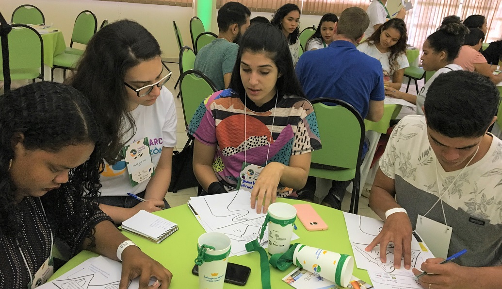 a group of people sitting at a table writing on paper