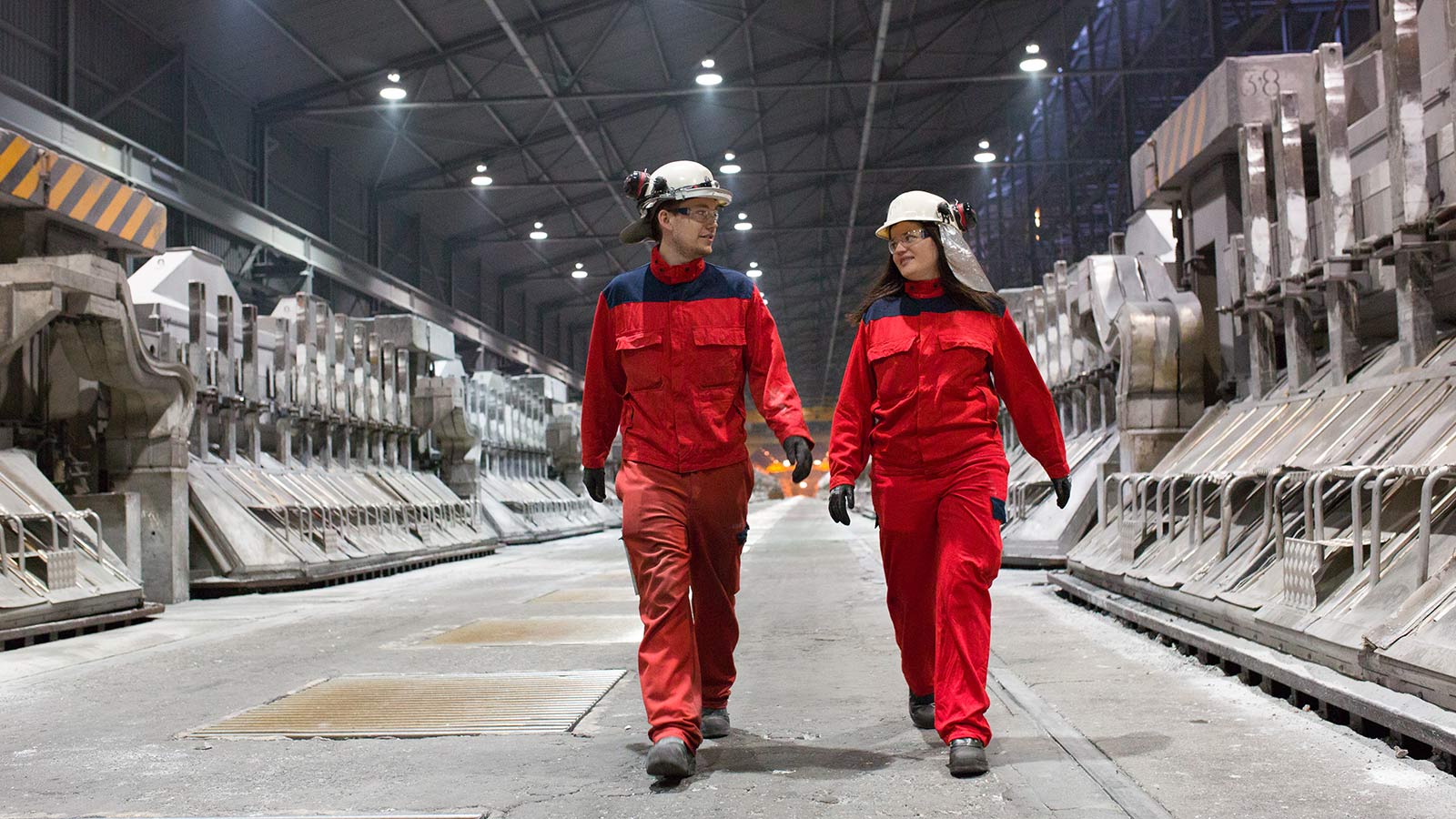 a man and woman wearing helmets and walking in a warehouse